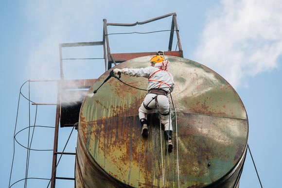 Worker suspended pressure washing rusty water tank