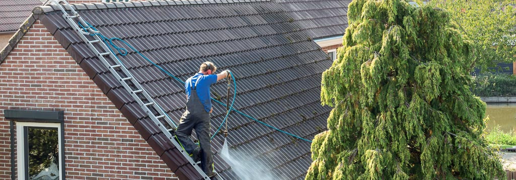 Worker pressure washing steep roof with ladder